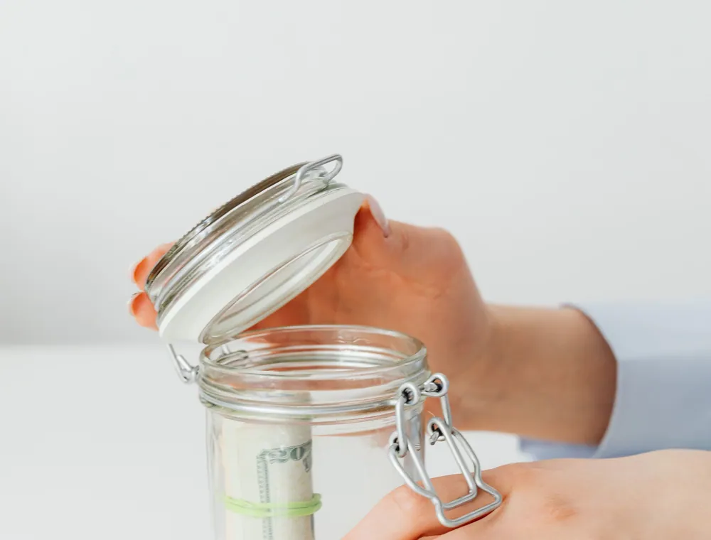 Hands putting savings into a glass jar